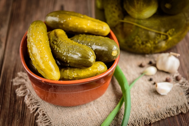 Eingelegte Gurken in der Schüssel auf rustikalem Holztisch mit Knoblauch und Glas Gurken.