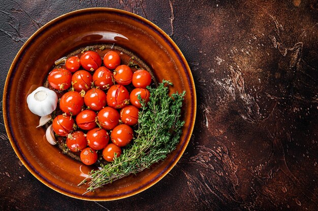 Eingelegte Kirschtomaten in einem rustikalen Teller mit Knoblauch und Thymian. Dunkler Hintergrund. Ansicht von oben. Platz kopieren.