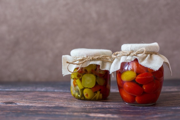 Eingelegte Kirschtomaten und eingemachter Gurkensalat in Gläsern auf Holzhintergrund