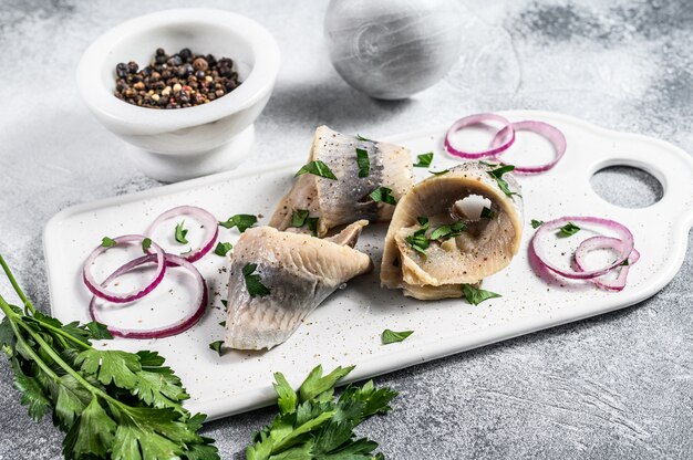 Eingelegter Hering mit Petersilie und roter Zwiebel. Grauer Hintergrund. Ansicht von oben