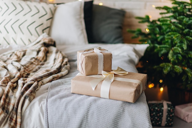 Eingepackte Weihnachtsgeschenke auf einem gemütlichen Bett neben dem Weihnachtsbaum mit schönen verschwommenen Lichtern