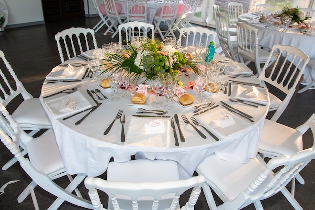 Eingerichteter festlicher weißer Hochzeitstisch mit Tellern und Gläsern und Blumenstrauß im Hochzeitsrestaurant