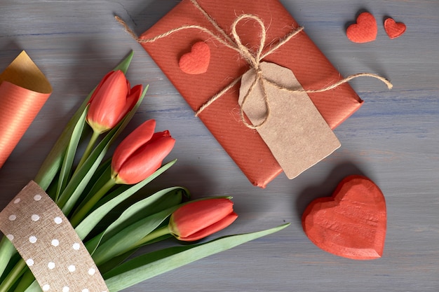 Eingewickelte rote Geschenk-Tulpen, Geschenkpapier und dekorative Herzen auf Holztisch