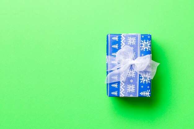 Eingewickeltes Weihnachts- oder anderes Weihnachtsgeschenk in Papier mit weißem Band auf grünem Hintergrund. Geschenkbox, Dekoration des Geschenks auf farbigem Tisch, Draufsicht mit Kopienraum.