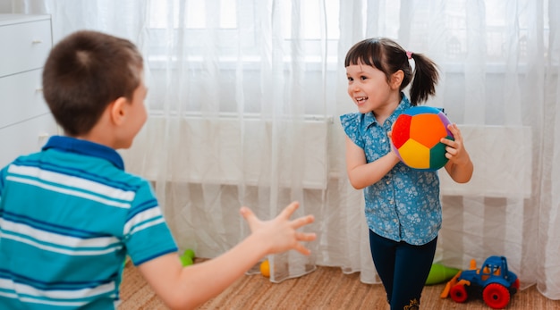 Einheimische Kinder, ein Junge und ein Mädchen, spielen in einem Kinderspielzimmer und werfen einen Ball