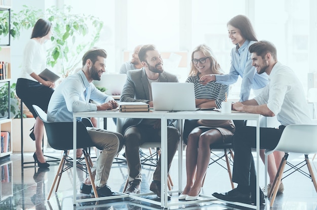 Einheit ist ein Schlüssel zum Erfolg. Gruppe junger Geschäftsleute, die zusammen arbeiten und kommunizieren, während sie am Schreibtisch sitzen, während die Kollegen im Hintergrund sitzen