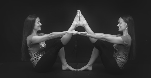 Einheitliche Zwillinge machen eine Yoga-Pose vor schwarzem Hintergrund