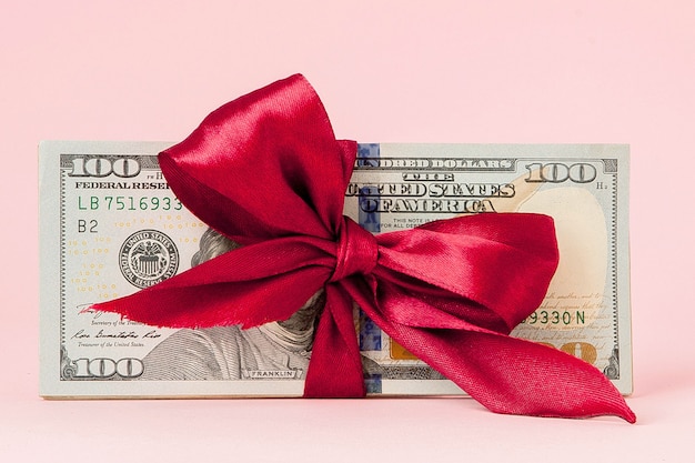Einhundert Dollar Geschenk mit einem roten Band auf rosa Tisch verpackt
