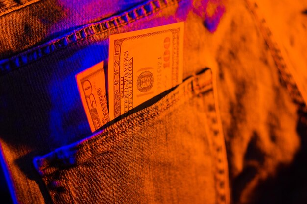 Einhundert Dollar in der Tasche einer blauen Jeans, Dollar im Neonlicht.