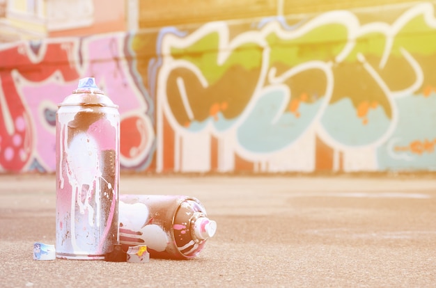 Einige benutzte Spraydosen mit rosa und weißer Farbe nahe der gemalten Wand in farbigen Graffitizeichnungen