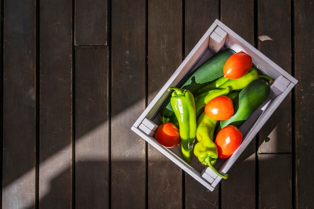 Einige frische Früchte und Tomaten mit italienischen grünen Paprika in einer Holzkiste, von oben gesehen und von einem Sonnenstrahl beleuchtet