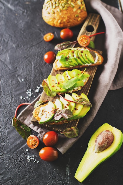 Einige geröstet mit grüner Avocado auf schwarzem Beton, vertikal