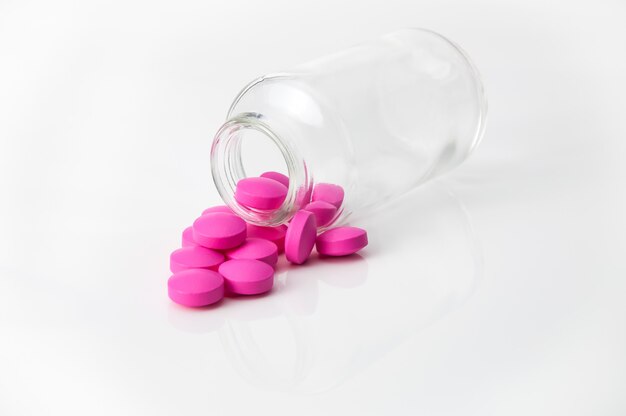 Einige große hellrosa Tabletten gossen aus einem Glasgefäß auf einen glatten weißen Hintergrund.