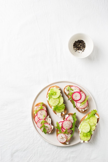 Einige Radieschen- und Gurkentoasts mit Ricotta und Salat mit Papier und Salz