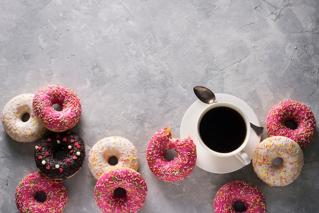 Einige rosa und weiße Donuts mit Tasse Kaffee über grauer Steinbeschaffenheit, Draufsicht, Kopienraum