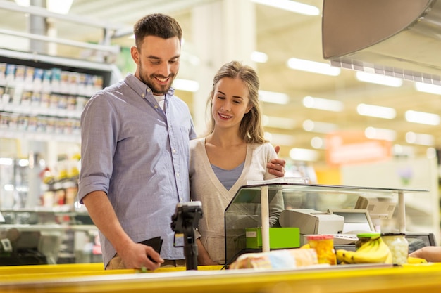 Einkaufen, Verkauf, Konsumismus und Menschenkonzept - glückliches Paar, das Lebensmittel im Lebensmittelgeschäft oder in der Supermarktkasse kauft