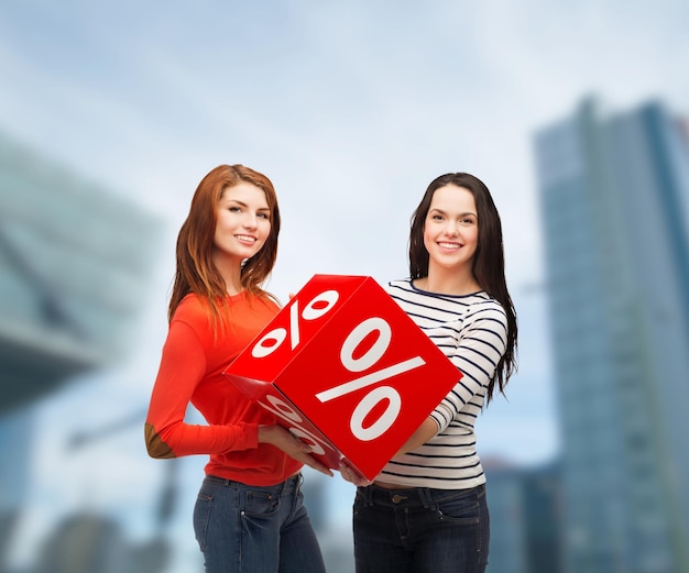 Einkaufen, Verkauf und Geschenk-Sconcept - zwei lächelnde Mädchen im Teenageralter mit Prozentzeichen auf roter Box im Freien