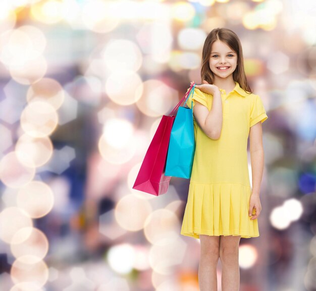 Einkaufs-, Glücks- und Menschenkonzept - lächelndes kleines Mädchen im gelben Kleid mit Einkaufstüten