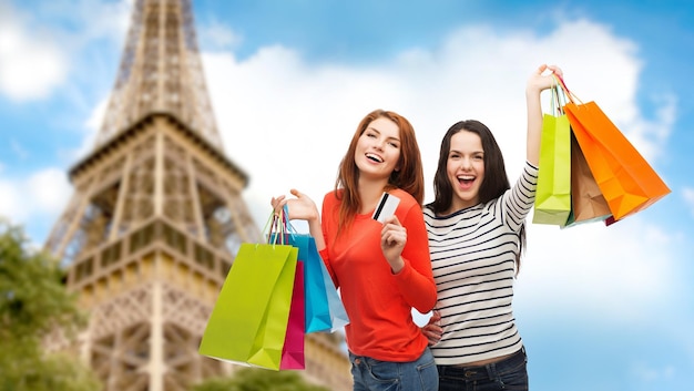 Einkaufs-, Verkaufs-, Tourismus- und Personenkonzept - zwei lächelnde Mädchen im Teenageralter mit Einkaufstüten und Kreditkarte über dem Hintergrund des Pariser Eiffelturms