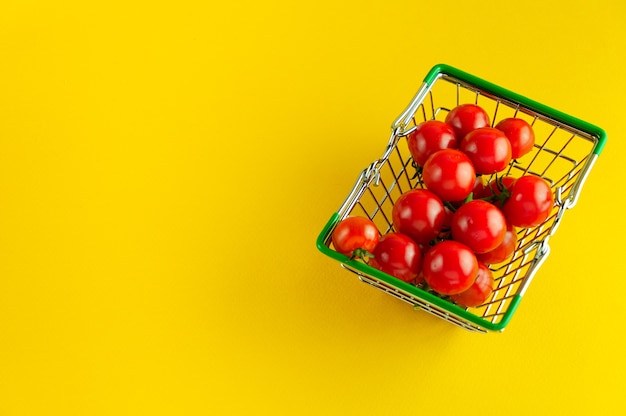 Einkaufskorb gefüllt mit Kirschtomaten auf einem leuchtend gelben Hintergrund