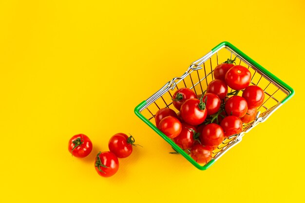 Einkaufskorb gefüllt mit Kirschtomaten auf einem leuchtend gelben Hintergrund