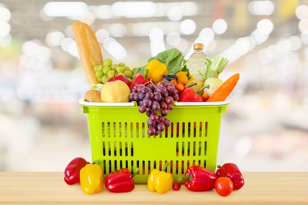 Einkaufskorb gefüllt mit Obst und Gemüse auf Holztisch mit Supermarkt Lebensmittelgeschäft verschwommen defokussiert