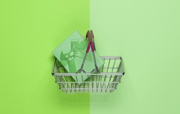 Einkaufskorb und Geschenkbox mit Bögen auf grünem Pastellhintergrund Zusammensetzung für Weihnachtsgeburtstag oder Hochzeit Draufsicht