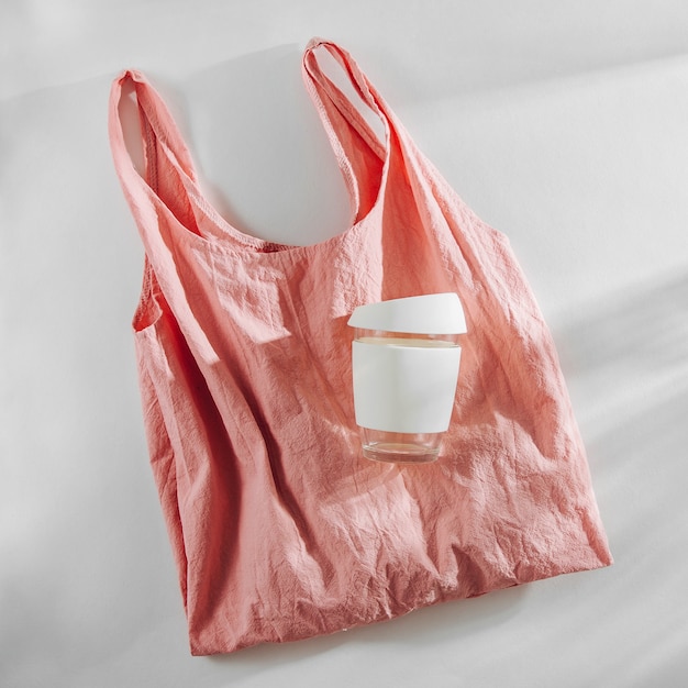 Einkaufstasche aus rosa Stoff und wiederverwendbare Kaffeetasse. Zero Waste, plastikfreies Konzept.