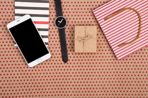 Einkaufstasche-Geschenkbox-Notizblockuhr und intelligentes Telefon auf Kraftpapierhintergrund in den roten Tupfen