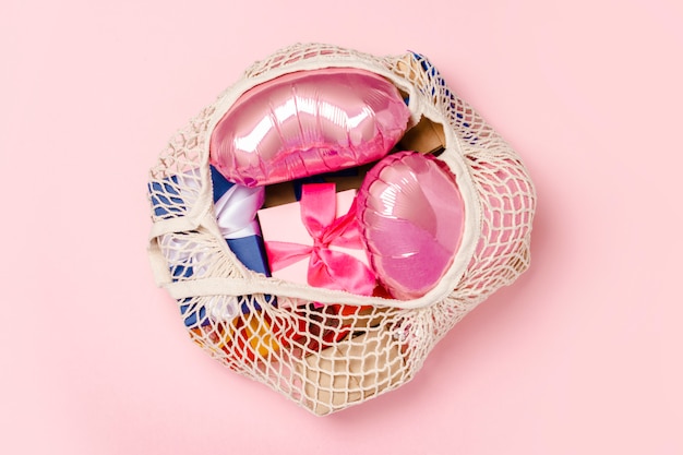 Einkaufstasche mit Geschenk und Herz formte Luftballon auf einer rosa Oberfläche. Geschenkkonzept für Familie, geliebte, Weihnachten, Valentinstag. . Flachgelegt, Draufsicht