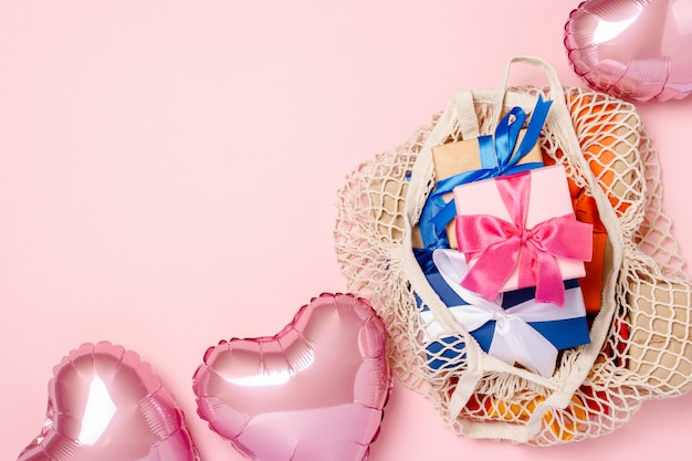 Einkaufstasche mit Geschenk und Herz formte Luftballon auf einer rosa Oberfläche. Geschenkkonzept für Familie, geliebte, Weihnachten, Valentinstag. . Flachgelegt, Draufsicht