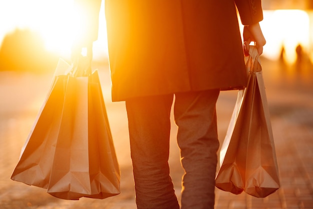 Einkaufstüten in den Händen bei Sonnenuntergang Hand des jungen Mannes mit Papiertüten mit Einkäufen