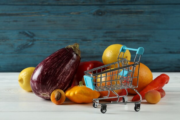 Einkaufswagen, Gemüse und Obst auf Holztisch