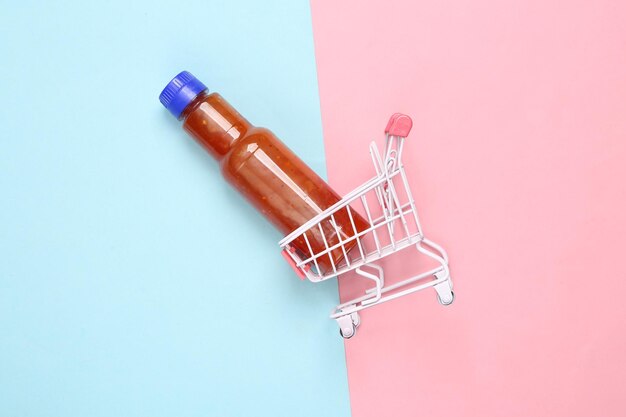 Einkaufswagen mit einer Flasche Tomatensauce Ketchup auf rosa-blauem Hintergrund