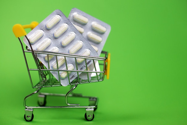 Einkaufswagen mit medizinischen Pillen auf grünem Hintergrund