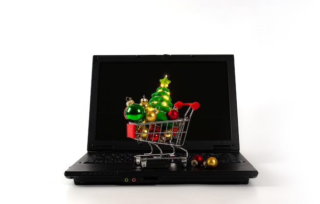 Einkaufswagen mit Weihnachtskugeln und Baum mit Girlanden auf dem Laptop Einfacher Hintergrund