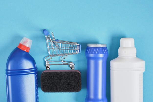 Einkaufswagen und Waschmittelflasche ohne Etiketten auf blauem Hintergrundreinigungsset. Ansicht von oben. Reinigungsservice-Konzept