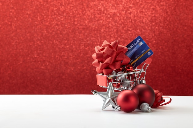 Einkaufswagen voll der Weihnachtsverzierungen auf rotem Hintergrund