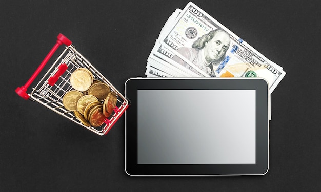 Einkaufswagengeld und Tablet-PC mit leerem Bildschirm auf schwarzem Hintergrund Top-Ansicht Kopierplatz