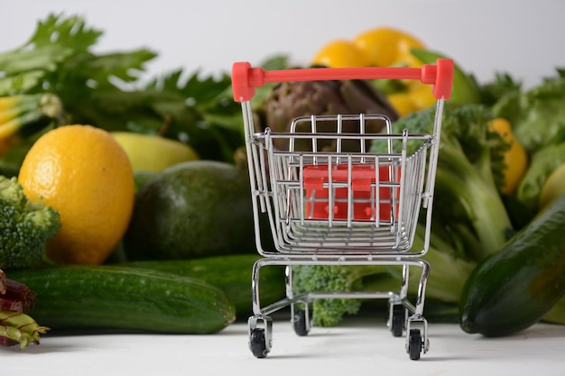 Einkaufswagenwagen und verschiedenes frisches Obst und Gemüse für das Layout Sortiment an frischem Obst und Gemüse Hintergrund für gesunde Lebensmittel Einkaufen von Lebensmitteln im Supermarkt