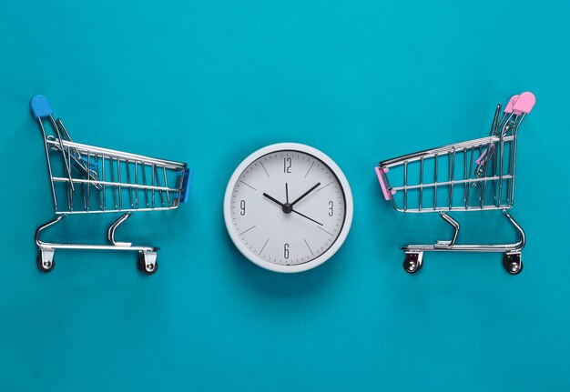 Einkaufszeit. Supermarktwagen mit Uhr auf blauem Hintergrund. Minimalismus. Draufsicht