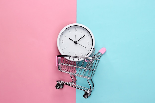 Einkaufszeit. supermarktwagen mit uhr auf rosa blauem hintergrund. minimalismus. draufsicht