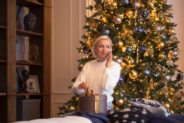 Einladung zur Neujahrsparty: junges Mädchen telefoniert nach dem Weihnachtsbaum dekorieren, Geschenke kaufen