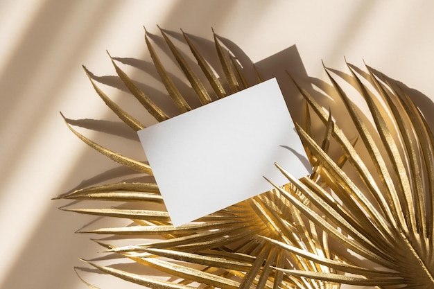 Einladungskartenmodell mit goldenen Palmblättern auf beigem pastellfarbenem Hintergrund Draufsicht flach liegender Kopierbereich Vorlage leer aus weißem Papier für Branding und Werbung