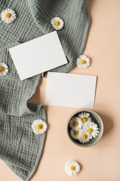 Einladungsvorlage im Flatlay-ästhetischen Pariser Stil Leere Papierblattkarte mit Mockup-Kopierbereich Kamille-Blütenknospen und Aquamarin-Musselin-Tuch auf neutralem beigem Hintergrund Flache Ansicht von oben