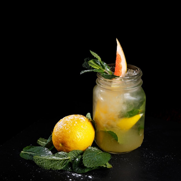 Einmachglas mit leckerer kalter Limonade, dekoriert mit Grapefruit-Zitrone und Minze auf schwarzem Hintergrund