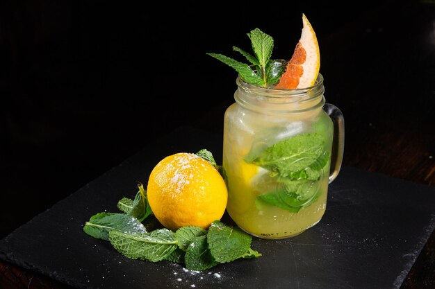 Einmachglas mit leckerer kalter Limonade, dekoriert mit Grapefruit-Zitrone und Minze auf schwarzem Hintergrund