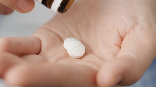 Einnahme von Pillen. Zwei große weiße runde Pillen fallen aus der Pillenflasche in die Handfläche. Nahaufnahme, Vorderansicht, Mittelkomposition