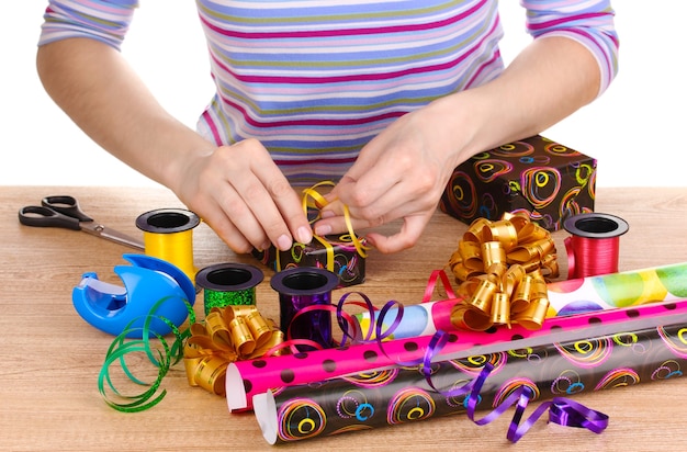 Einpacken von Geschenken umgeben von Papier, Bändern und Schleifen