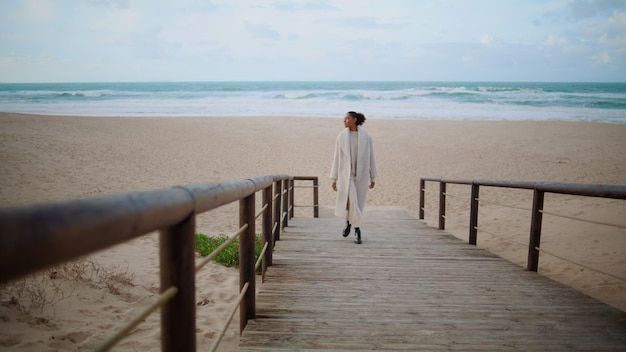 Einsame Frau, die am Strand spazieren geht, auf einem hölzernen Pfad, ruhig, afrikanisch-amerikanisch, genießt die Zeit.